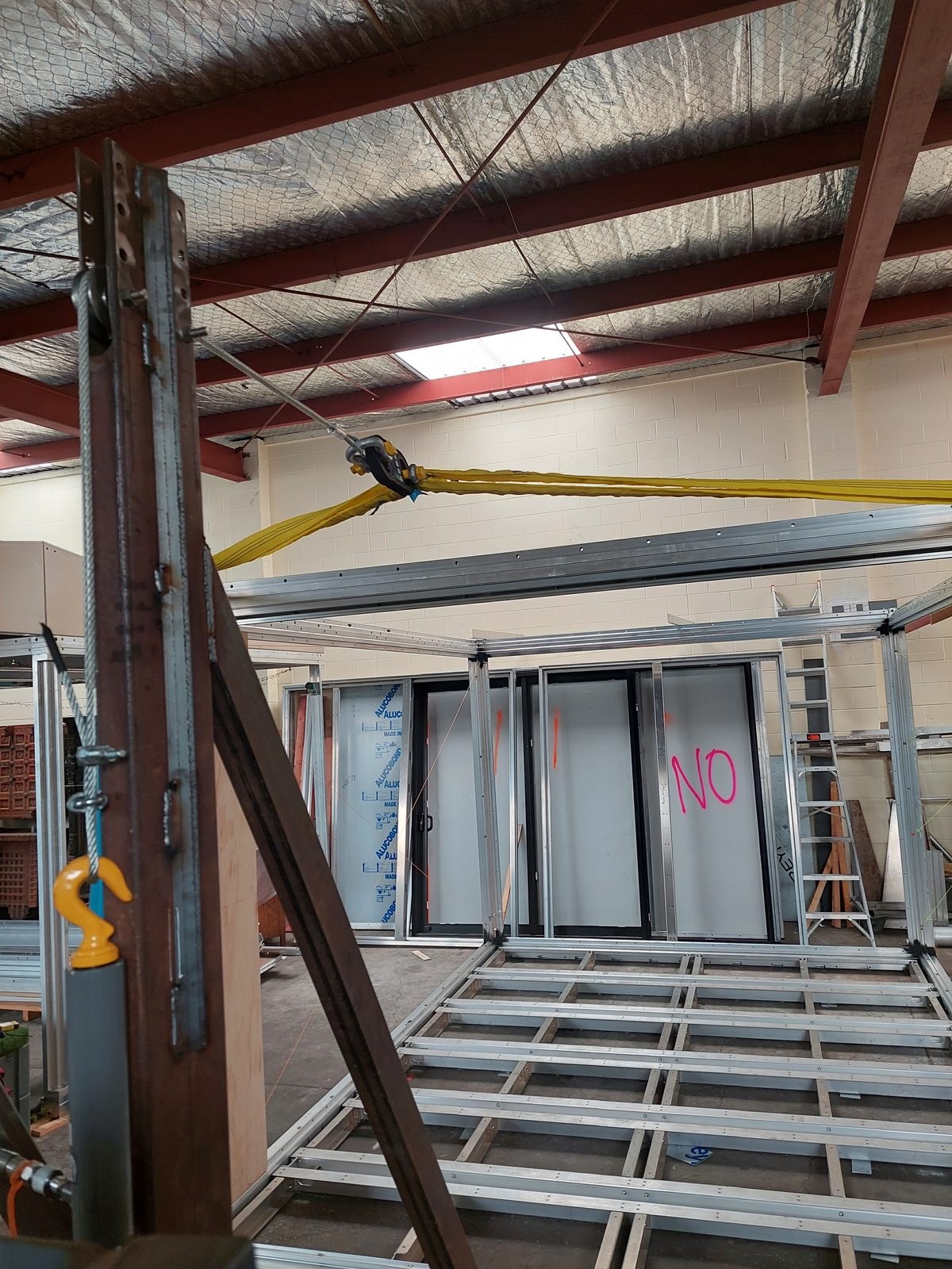 Anyplace module suspended under live load test, 2024 — yellow rigging strap visible from overhead structural beam, full module construction visible below